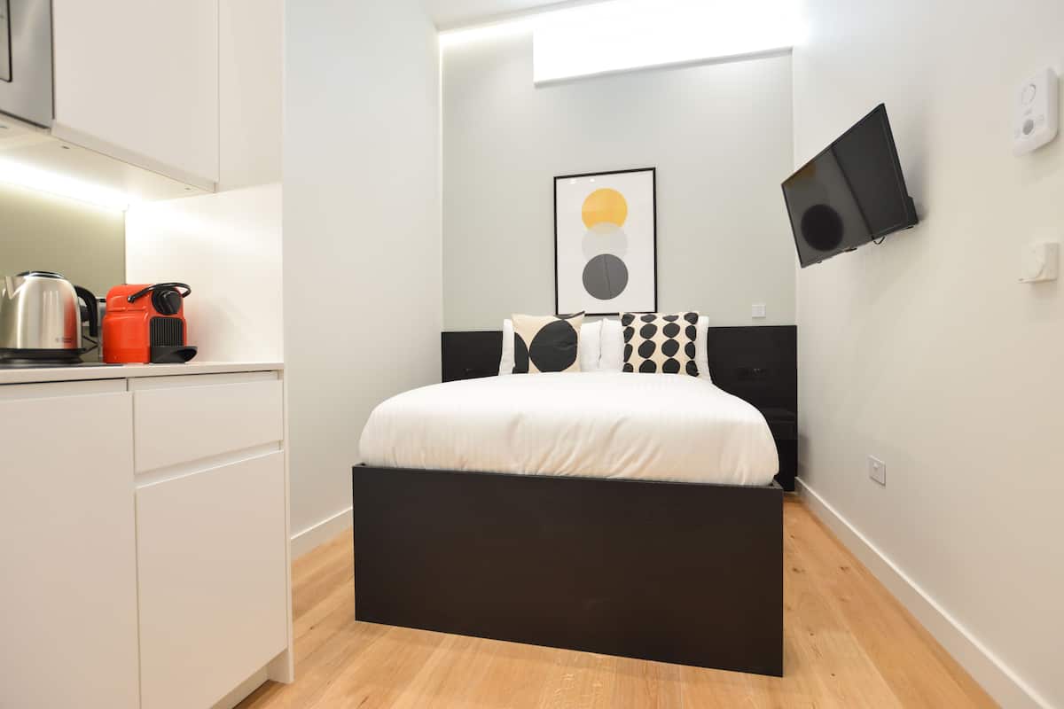 Ein modernes Schlafzimmer mit Bett, Flachbildfernseher und Küchenzeile mit Wasserkocher und Toaster.