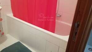 A bathroom with a white bathtub, a red shower curtain, and a green mat. - Nice Apartment s+2 Menchia hammem sousse (Hammam Sousse)