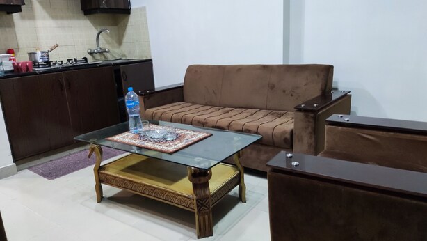 A living room with a glass coffee table, a brown sofa, and a wooden cabinet. - Private & Secure 1BHK Flat - Central location Ph7 (Rawalpindi)