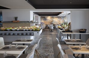 A modern restaurant with a buffet area, white tables, and chairs. - Hotel Brisamar Suites (El Vendrell)