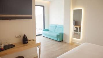 Habitación de hotel moderna con una televisión de pantalla plana, un escritorio de madera con un hervidor, un sofá azul claro y una cama.