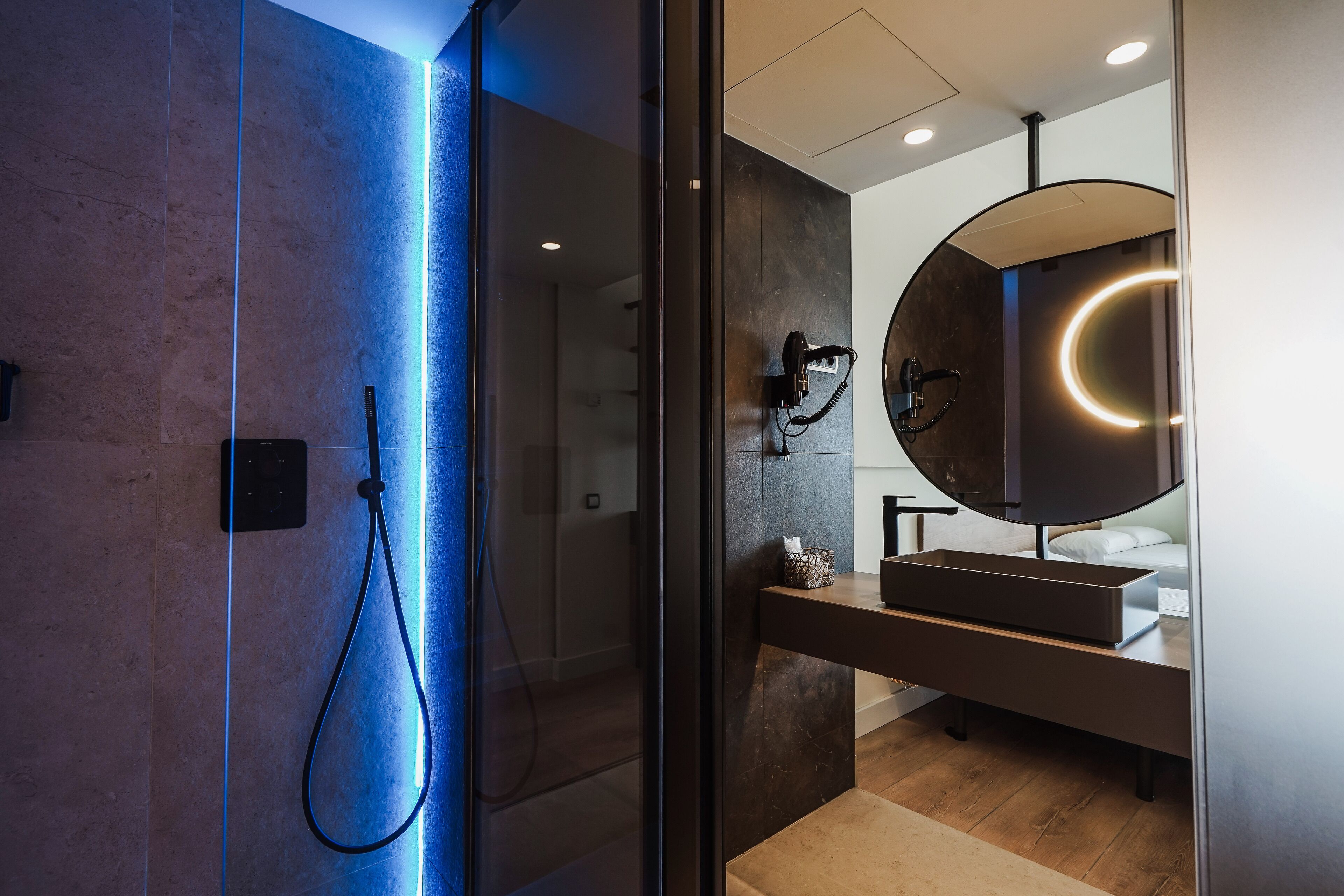 A modern bathroom with a glass-enclosed shower, a round mirror with a circular light, and a wooden vanity.