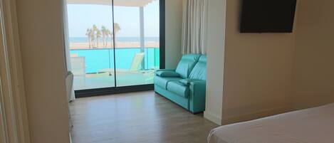 A hotel room with a balcony, a teal sofa, a bed, and a TV on the wall.