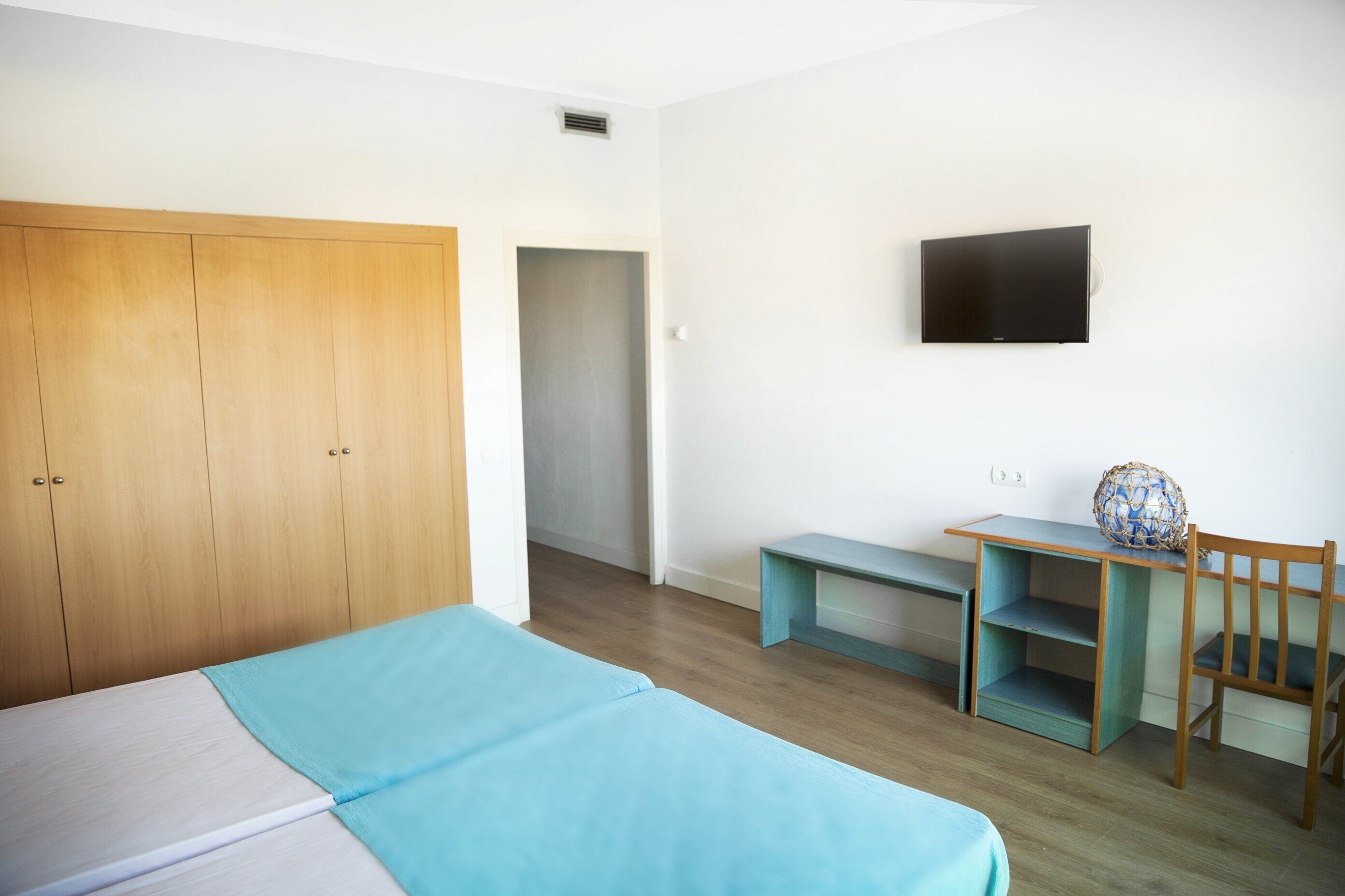 Une chambre à coucher avec un lit, une armoire en bois, un bureau avec une chaise et un téléviseur fixé au mur.
