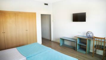 Une chambre à coucher avec un lit, une armoire en bois, un bureau avec une chaise et un téléviseur fixé au mur.