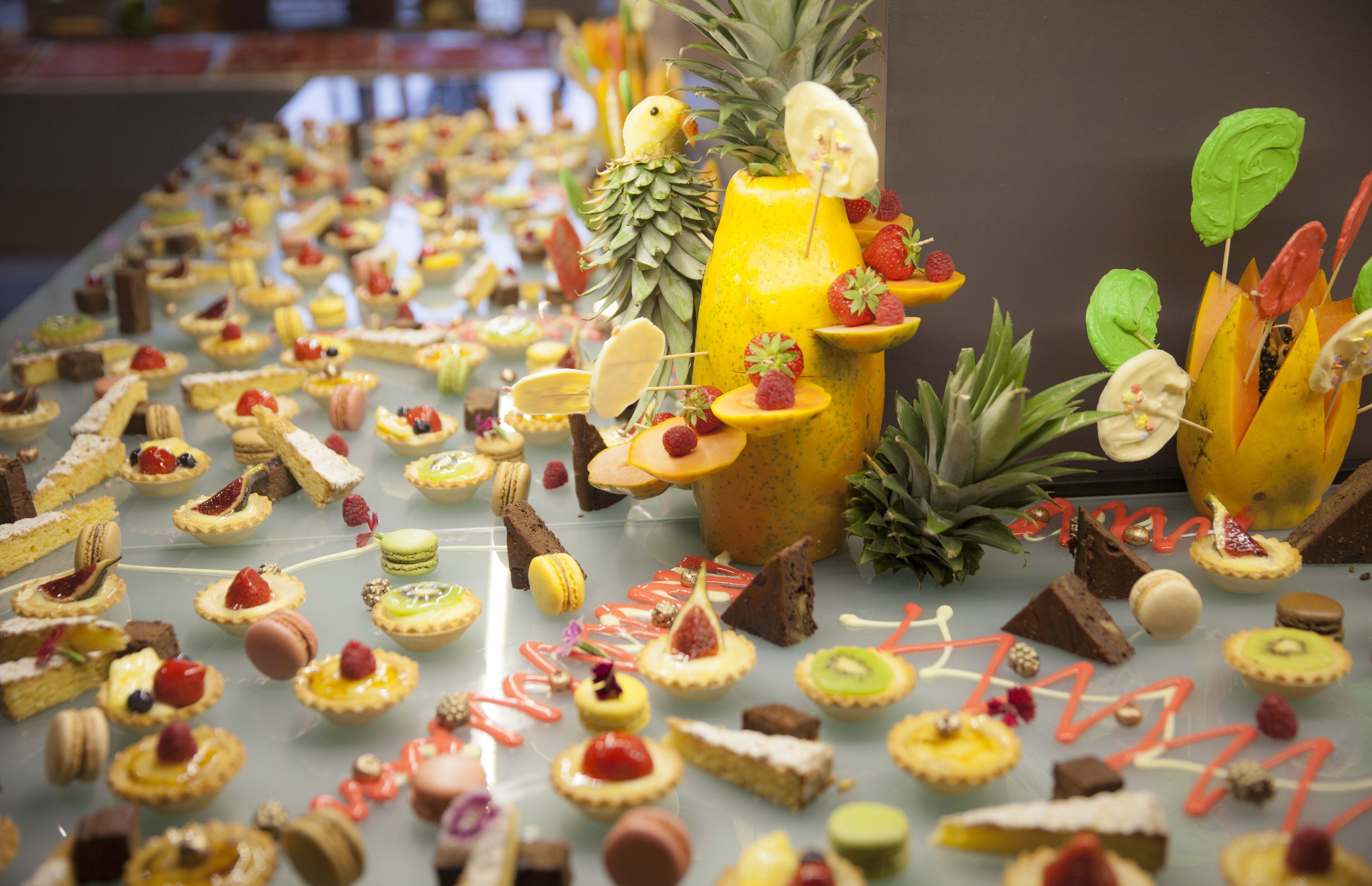 Verschiedene Desserts sind auf einem Tisch angerichtet, darunter Macarons, Törtchen und Fruchtdekorationen.