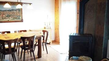 Een gezellige woonkamer met een houten plafond, een eethoek met een houten tafel en stoelen, en een open haard.