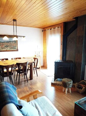 A cozy living room with a wooden ceiling, a dining area with a wooden table and chairs, and a fireplace.