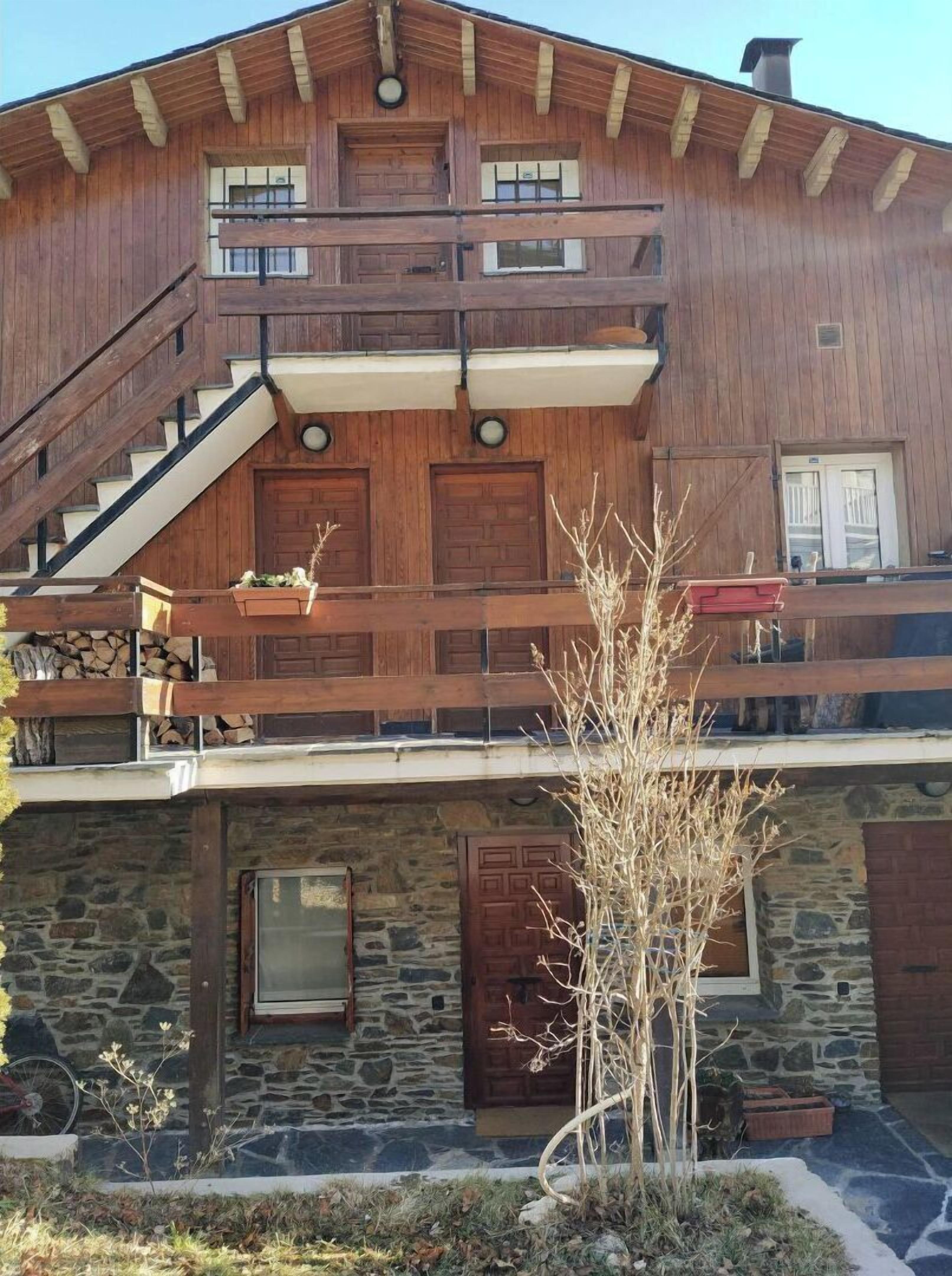 A two-story wooden house with a stone foundation, a wooden staircase, and a balcony with a railing.