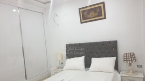 Un dormitori amb un llit, dues taules de nit, una tauleta solera, una làmpada penjada a la paret i un objecte emmarcat a la paret.