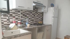 Una cocina con pileta, estufa y refrigerador. Hay alacenas, una encimera y un salpicadero de azulejos.