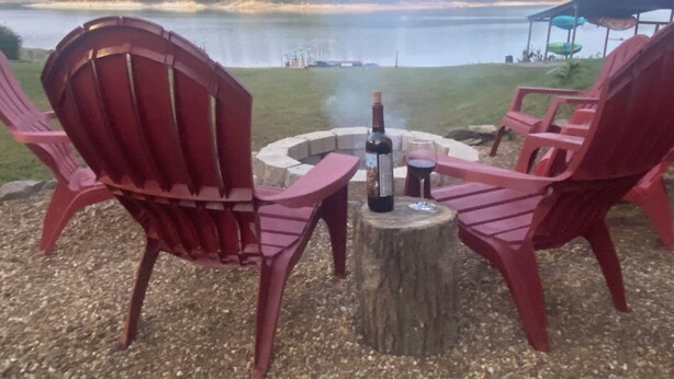 A lakeside seating area with Adirondack chairs and a fire pit.