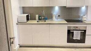 A modern kitchen with white cabinets, a stainless steel sink, a Bosch oven, and a microwave. - Stunning 1-bed Deluxe Apartment in Slough (Slough)