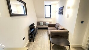 A modern living room with a sofa, a coffee table, a TV, and a mirror. - Stunning 1-bed Deluxe Apartment in Slough (Slough)