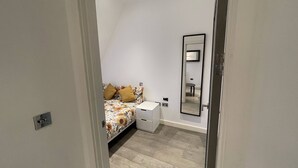 A bedroom with a bed, a bedside table, a mirror, and a light switch on the wall. - Stunning 1-bed Deluxe Apartment in Slough (Slough)