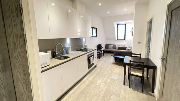 A modern kitchen with white cabinets, a built-in oven, and a dining area with a table and chairs. - Stunning 1-bed Deluxe Apartment in Slough (Slough)