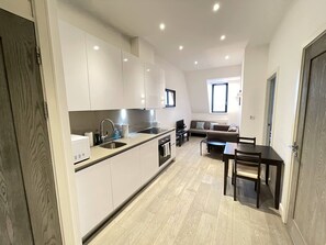 A modern kitchen with white cabinets, a built-in oven, and a dining area with a table and chairs. - Stunning 1-bed Deluxe Apartment in Slough (Slough)