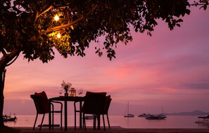 A table set for two under a tree with a sunset view.