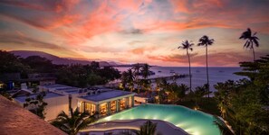 A resort with a swimming pool, beachfront views, and a sunset sky.