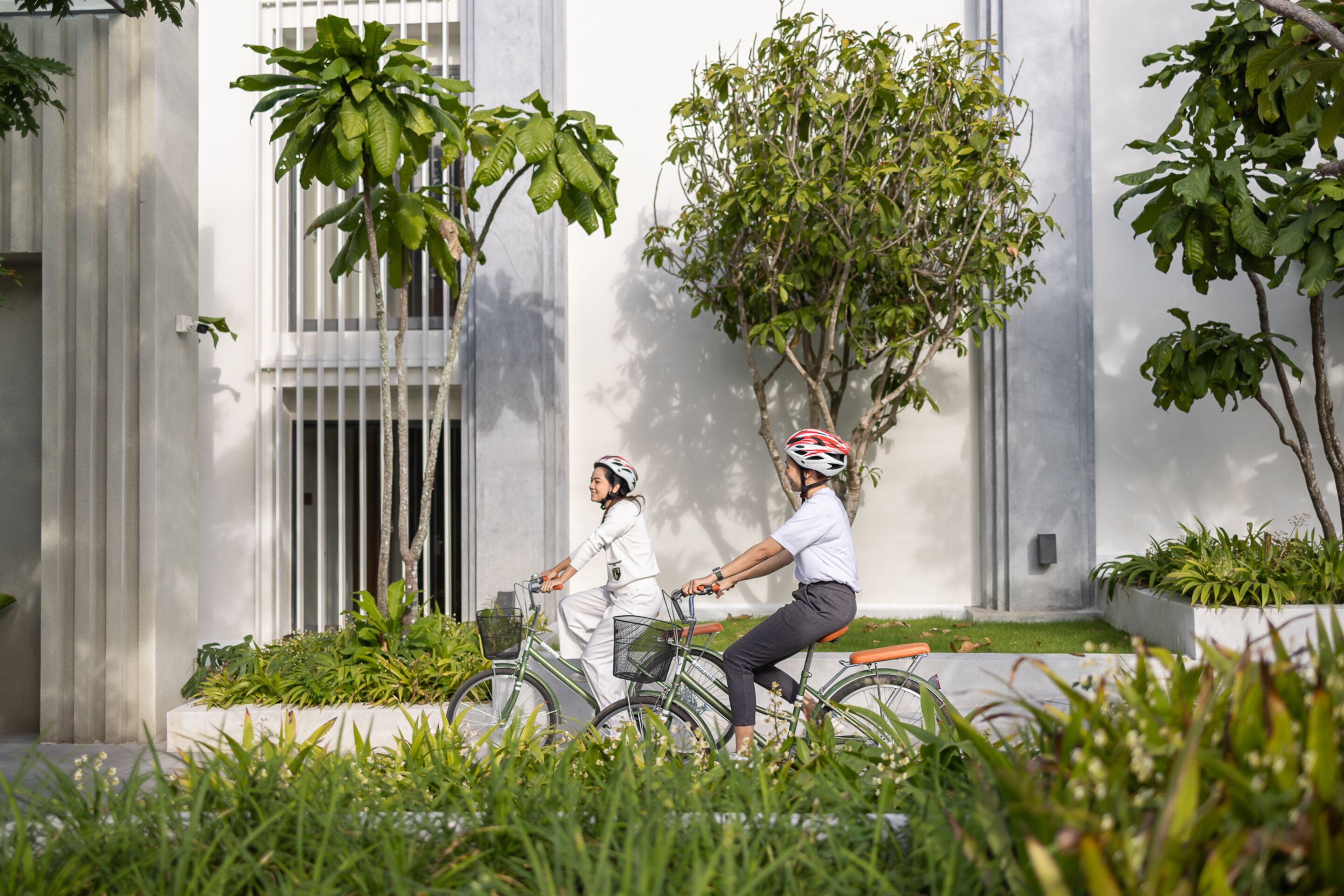 Twee personen fietsen in een binnenplaats met een modern gebouw op de achtergrond.