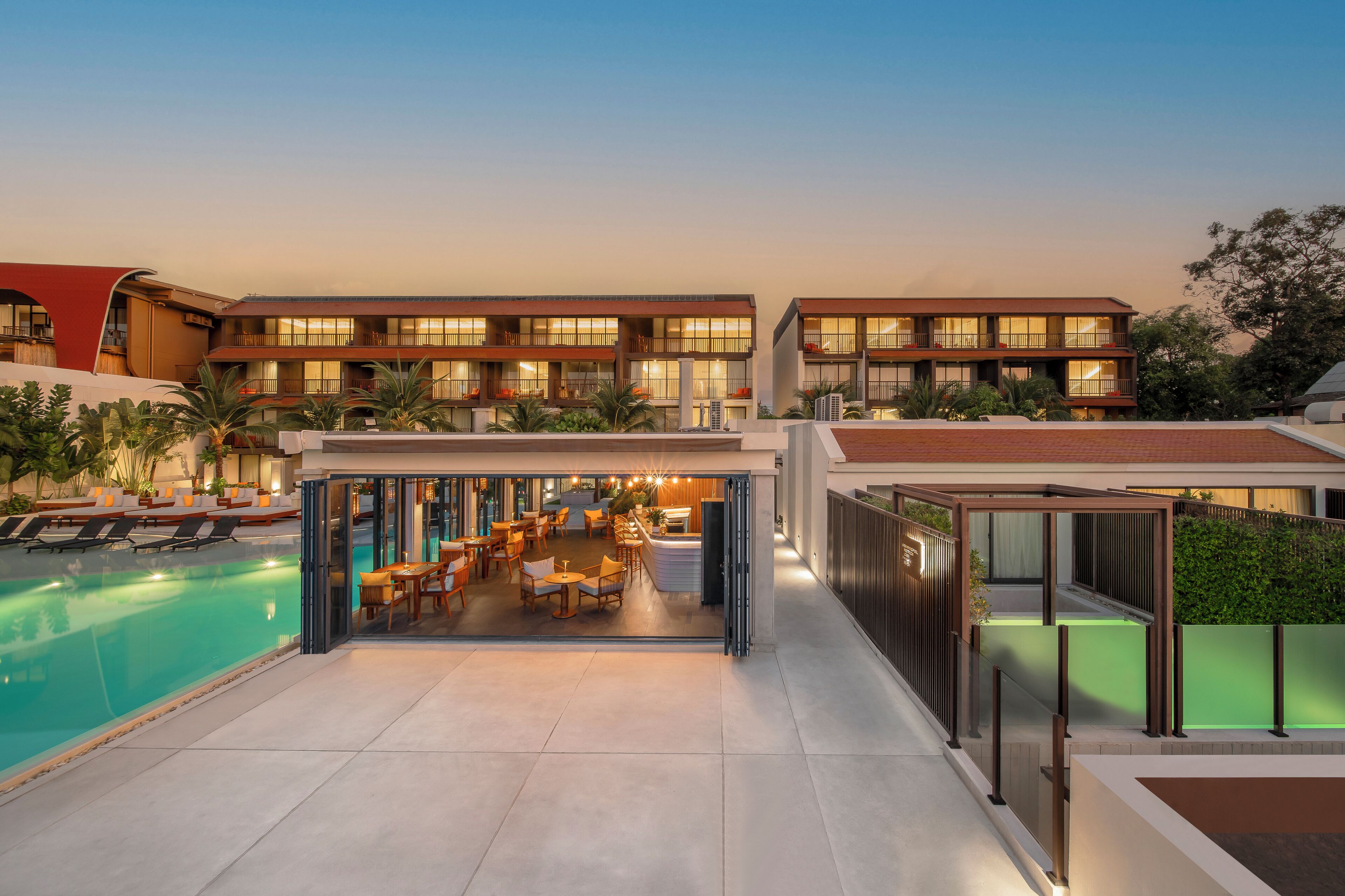 A modern hotel with a swimming pool, outdoor seating, and a covered dining area.