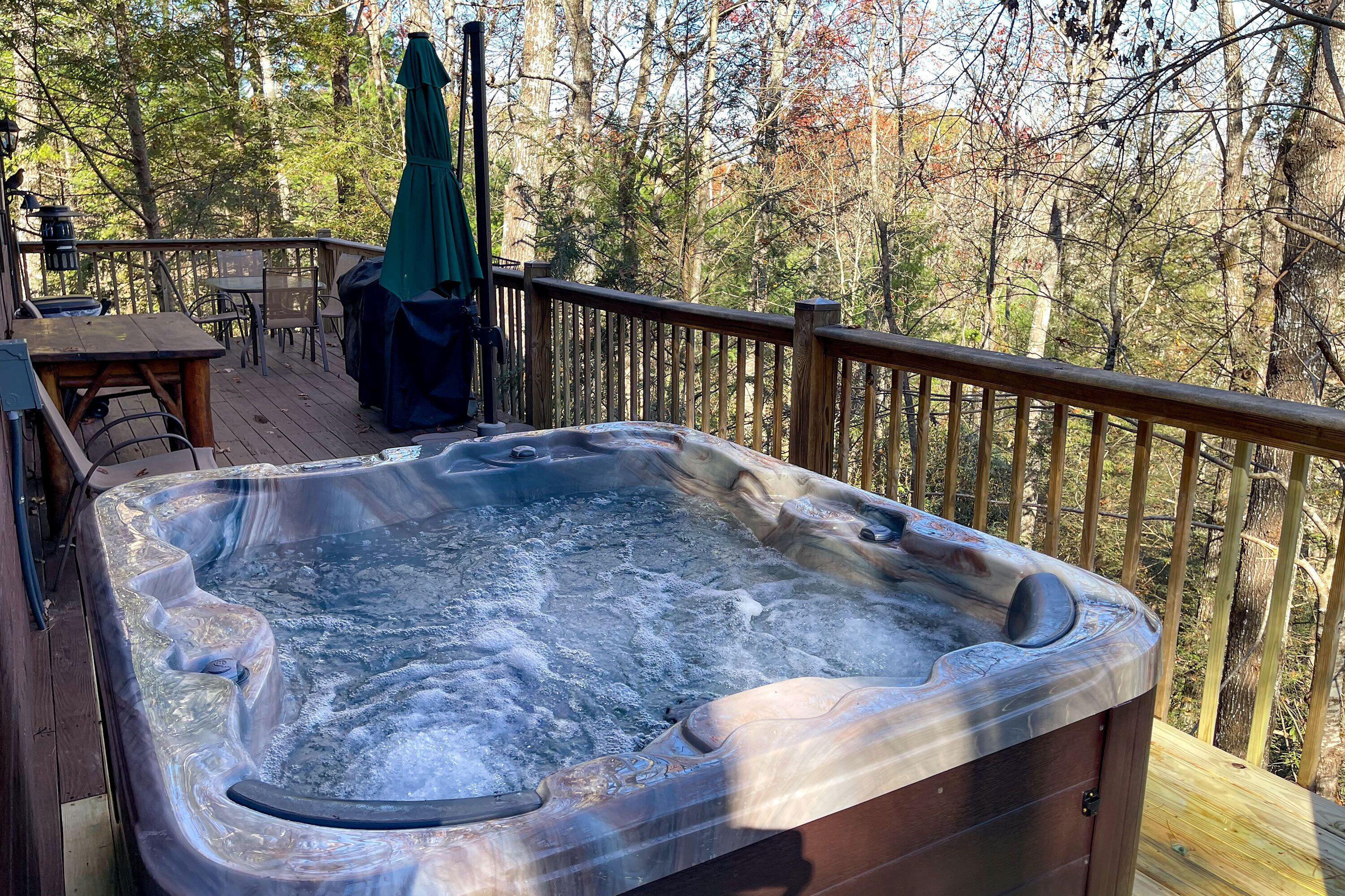 A hot tub on a wooden deck with a view of trees.