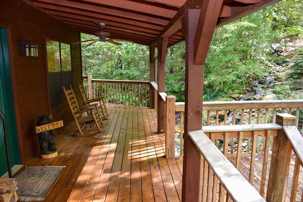 A wooden deck with a welcome sign, a bench, and a view of a forested area.