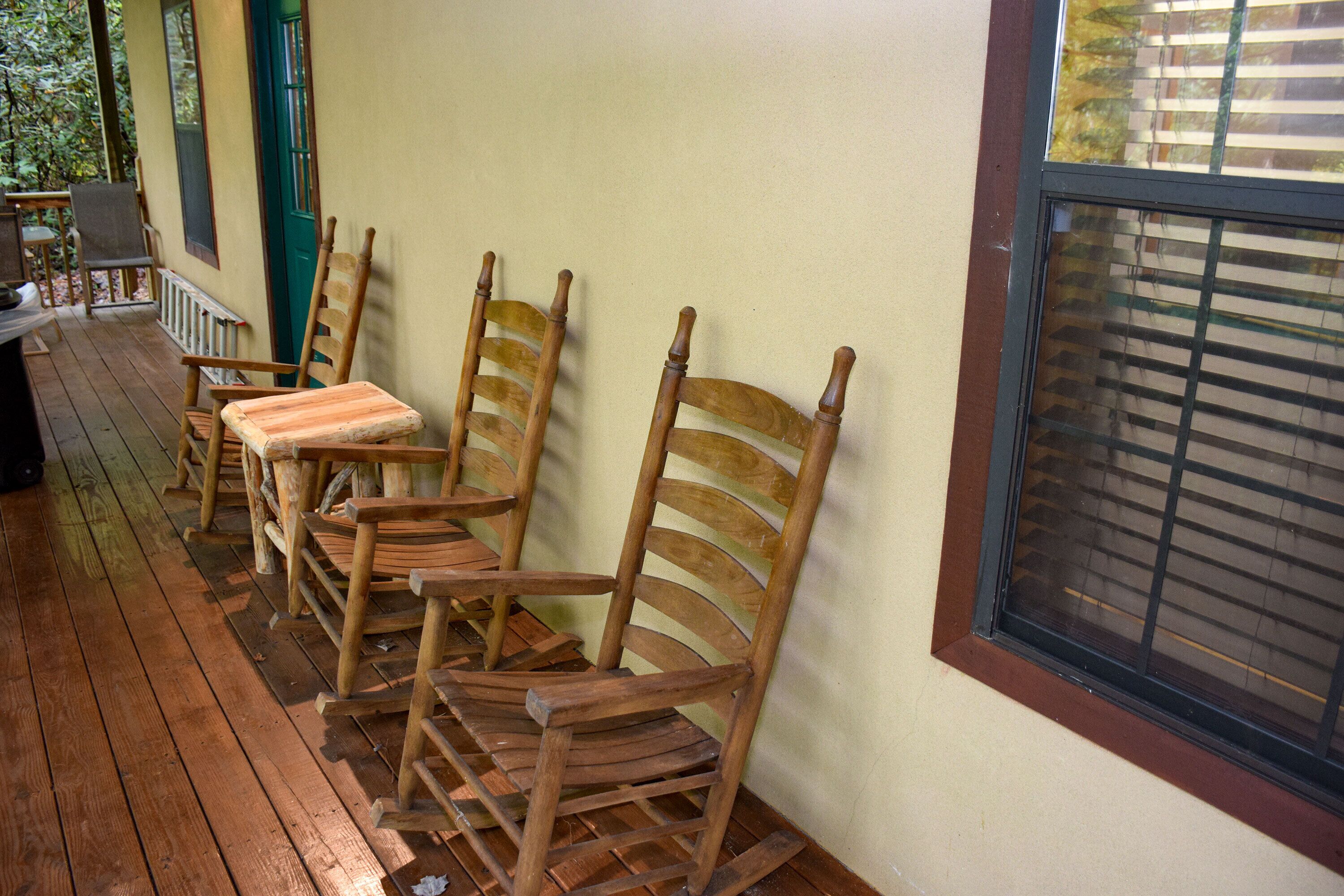 A porch with wooden rocking chairs and a window with blinds.