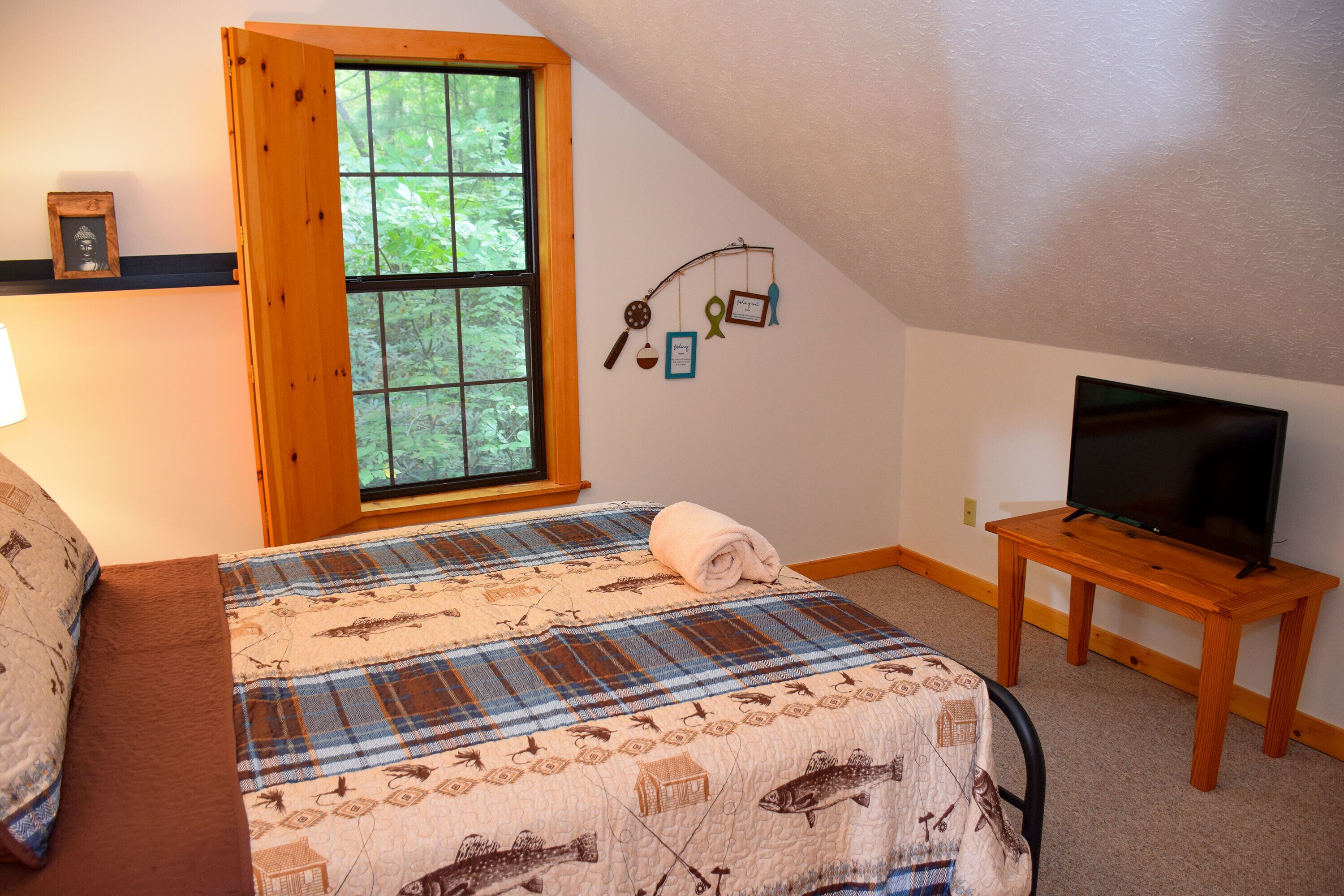 A bedroom with a bed, a window, a television on a wooden table, and a wall decoration.
