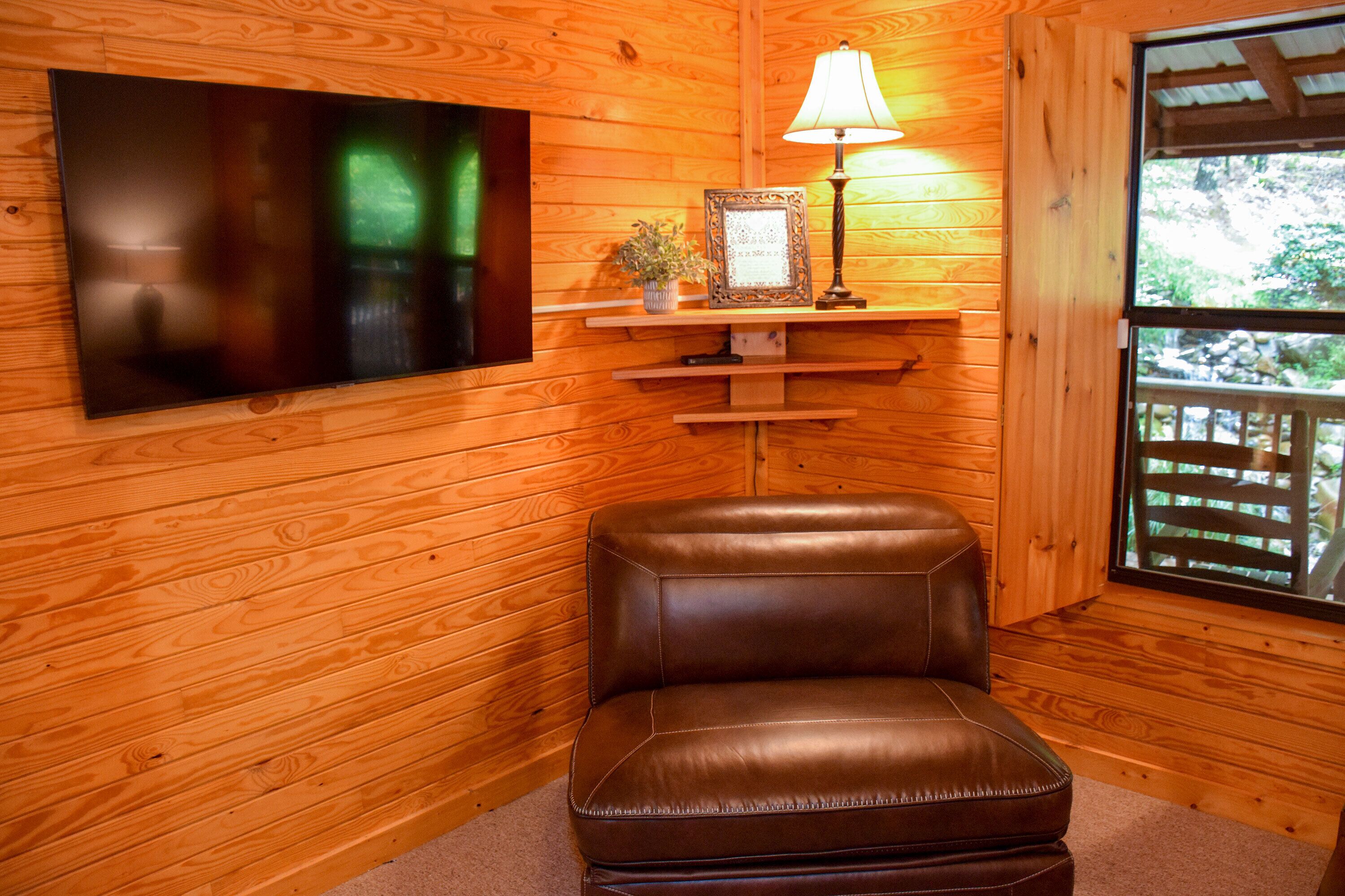 A wooden interior with a leather chair, a framed picture, a lamp, and a TV on the wall.