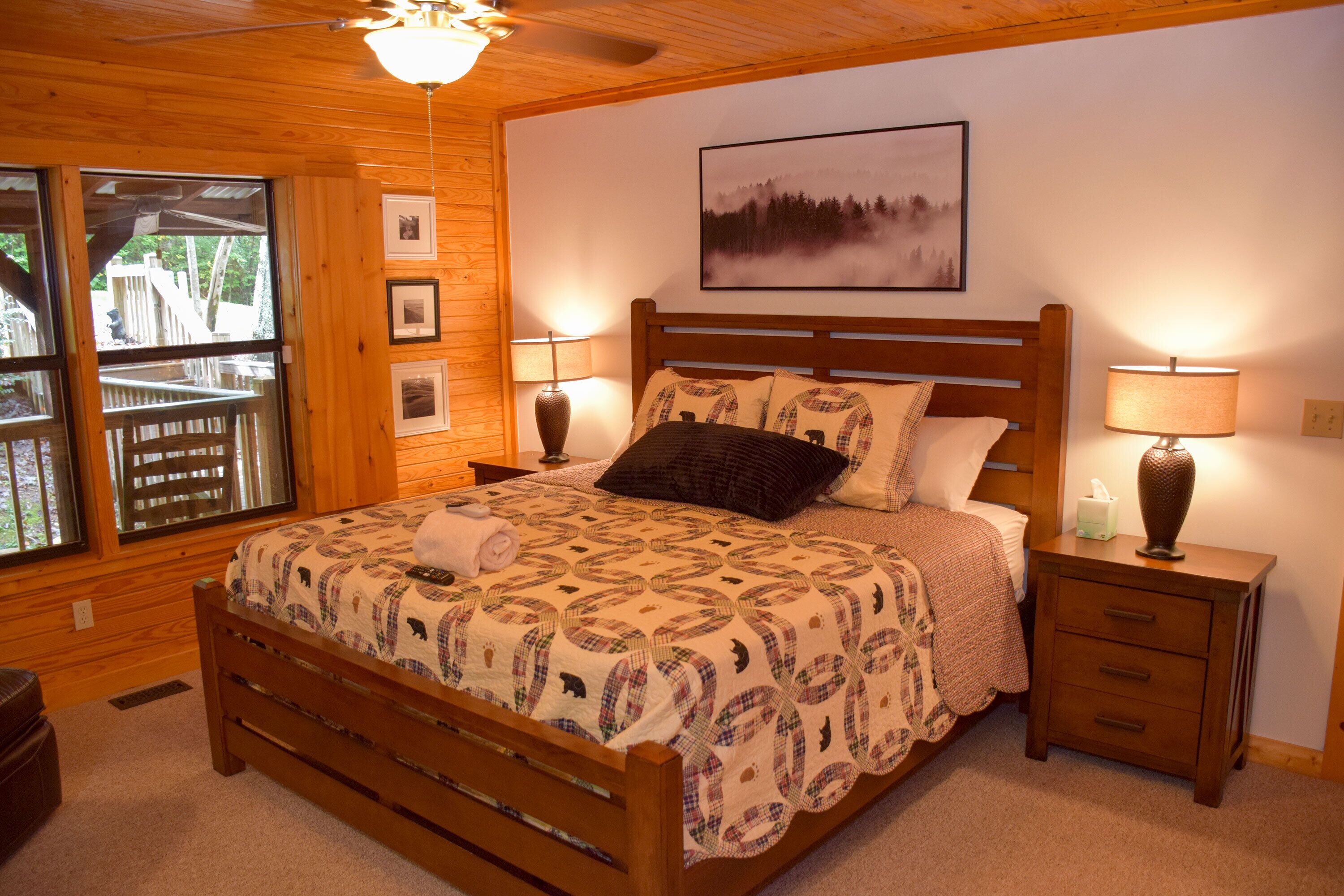 A wooden-framed bed with a quilt, two bedside lamps, and a framed picture on the wall.