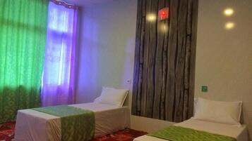 Two single beds with green bedspreads and white pillows, set against a patterned carpet and a wall with a vertical panel design.
