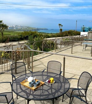 An outdoor seating area with a round table and chairs, a tray with cups and a banana, and a view of the coastline. - 8 Zinc - an apartment that sleeps 4 guests in 2 bedrooms (Newquay)
