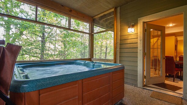Un jacuzzi en una cabaña de madera con vistas a árboles a través de amplios ventanales.