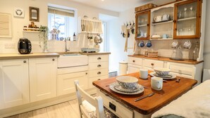 A modern kitchen with white cabinetry, a wooden dining table, and a breakfast bar. - Cartrefle (Bala)