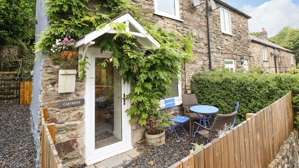 A stone cottage with a small garden, a wooden fence, and a blue chair outside. - Cartrefle (Bala)