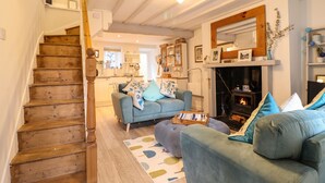 A cozy living room with a staircase, a fireplace, and a kitchen in the background. - Cartrefle (Bala)