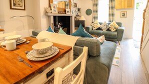 A cozy living room with a dining area, a fireplace, and a sofa with cushions. - Cartrefle (Bala)