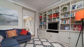 Un salon avec un canapé bleu, un tapis à motifs, une bibliothèque et un téléviseur.