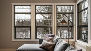 Ein Zimmer mit grauem Ecksofa, mehreren Fenstern und einer Stehlampe.