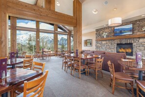 A spacious dining area with wooden tables and chairs, a stone fireplace, and large windows offering mountain views.
