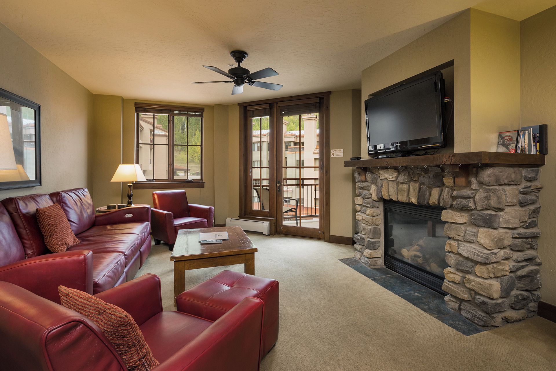 A living room with a stone fireplace, leather sofas, a television, and a ceiling fan.