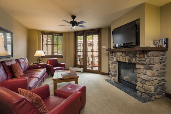 A living room with a stone fireplace, leather sofas, a television, and a ceiling fan.