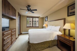 A hotel room with a bed, a desk, a TV, a ceiling fan, and a window.