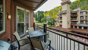 Een balkon met een tafel en stoelen, met uitzicht op het dorpscentrum, met gebouwen en een beboste heuvel.