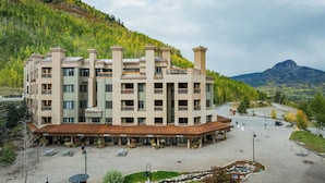Een meerlaags hotel met balkons, een overdekt terras en uitzicht op een bergachtig landschap.