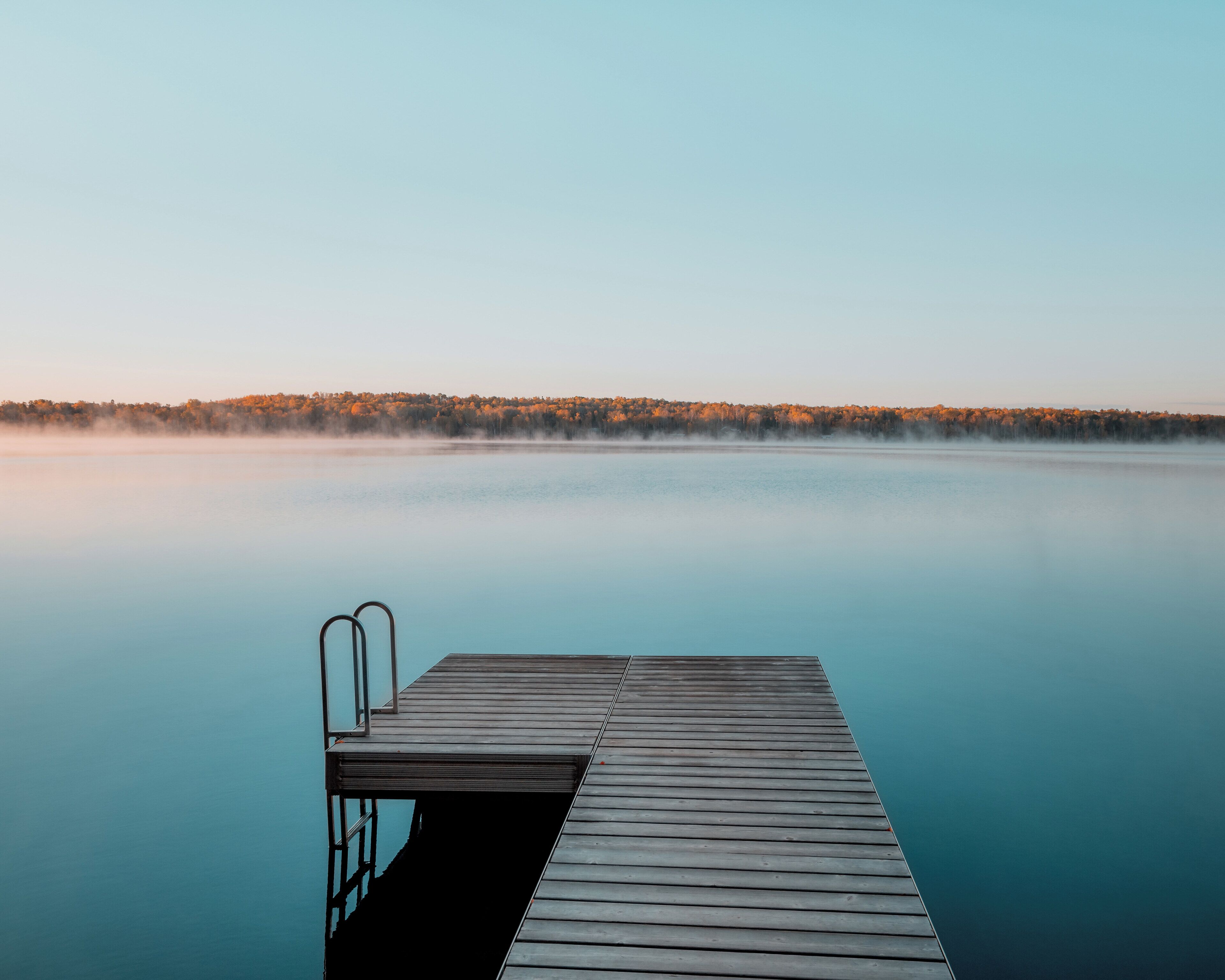 A wooden dock extending into calm water with a forested shoreline in the background.