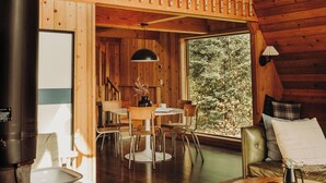 A wooden cabin interior with a dining area, a sofa, and a large window overlooking trees. - The Minne Stuga  (Grand Marais)