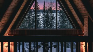A cabin with a large triangular window, wooden beams, and a view of a snowy landscape. - The Minne Stuga  (Grand Marais)