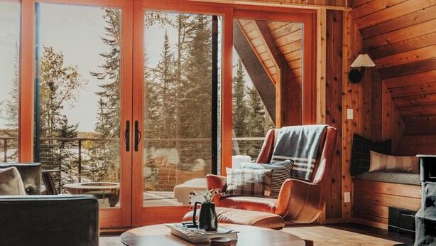 A spacious room with a large sliding glass door leading to a balcony, a cozy seating area with a sofa and chairs, and a small table with a book and a vase. - The Minne Stuga  (Grand Marais)
